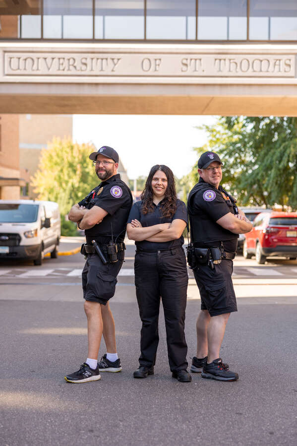 Public Safety Officers Sgt. Mitch Lucius, Sgt. Rachel Smart (Administrative Staff), and Ofc. Luke Anderson pose for a group photo under a skyway that says St. Thomas on Aug. 28, 2025 in St. Paul.