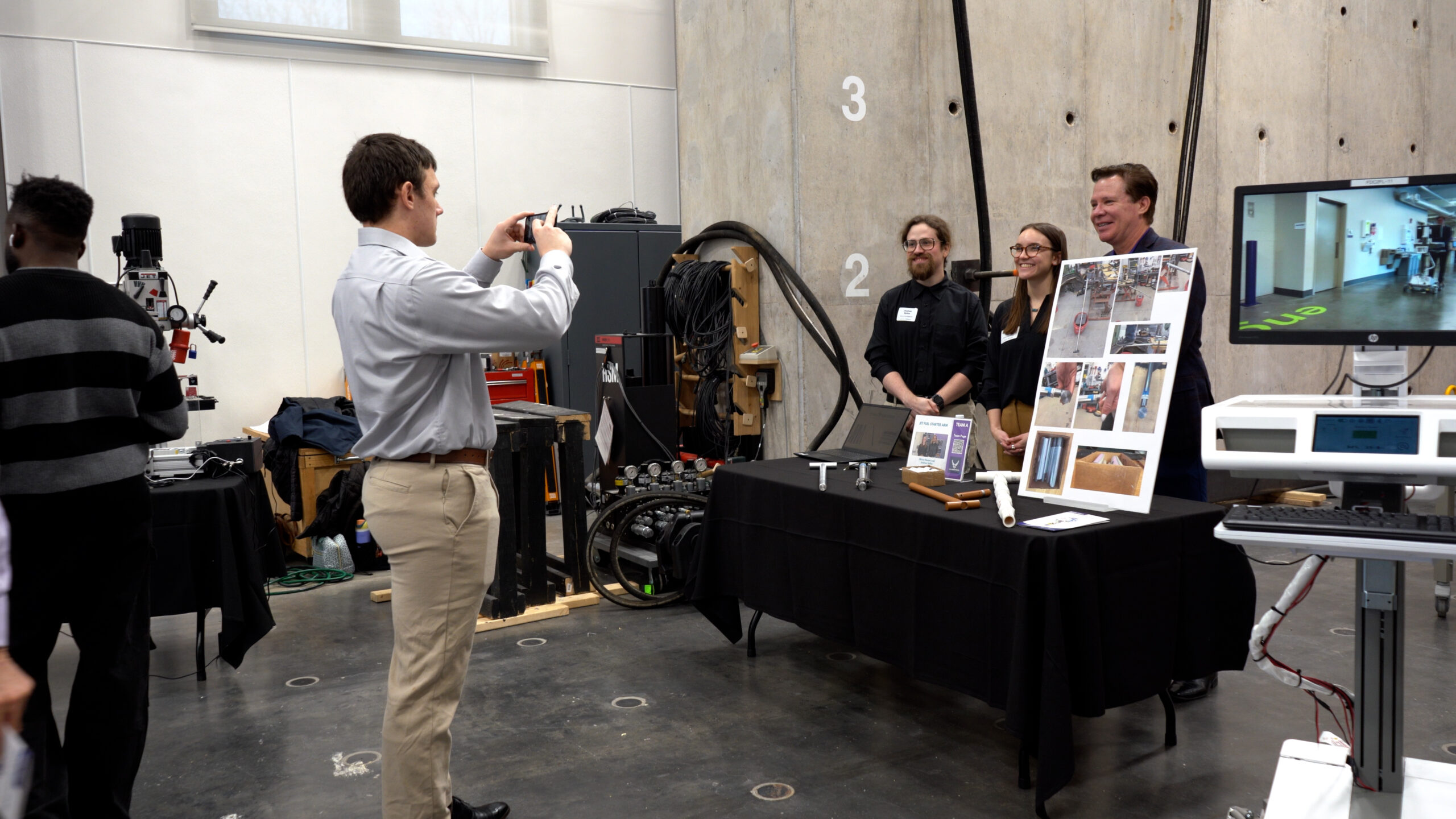Three people take a group photo by their project.