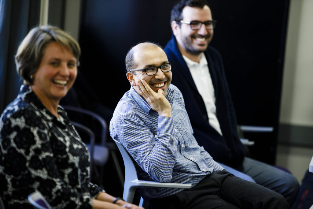 Three people sitting next to each other and Kundan Nepal in the middle looking ahead laughing.
