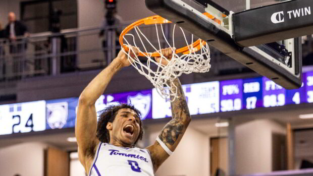 Tommies basketball athlete hanging on the rim.