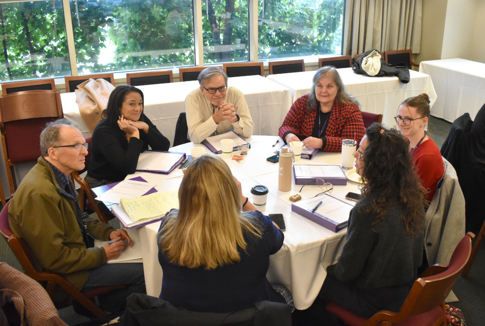 A group of seven people sit and talk at a table together.