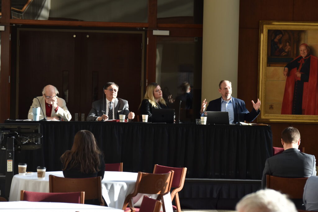 Four speakers sit at a table facing the audience.
