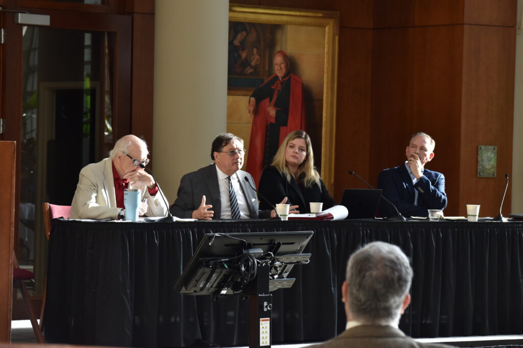 Four speakers sit at a table facing the crowd.