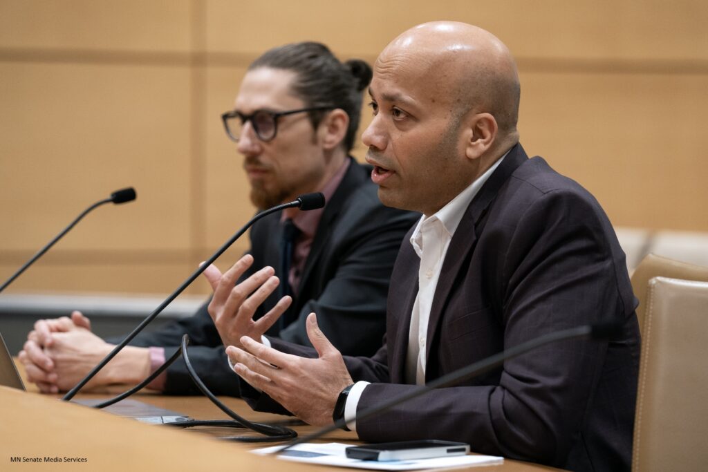 Two men sit next to each other in front of a microphone.