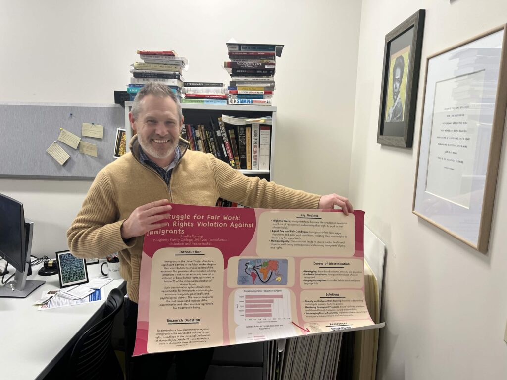A man smiles while holding up a large pink poster.
