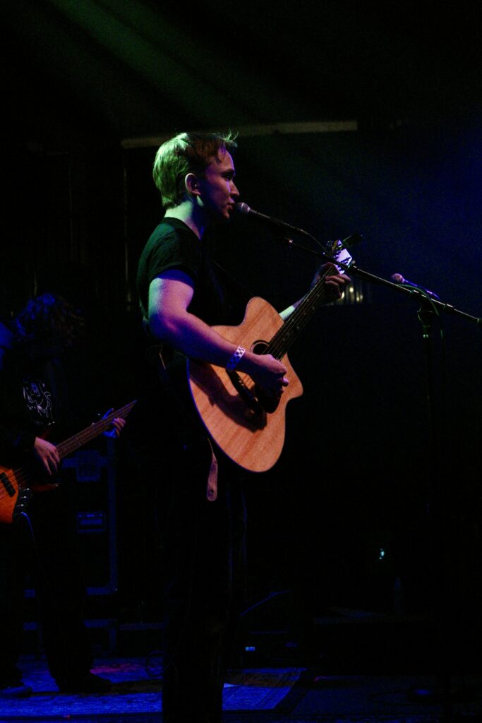 Benjamin Barrett sings on stage with a guitar.