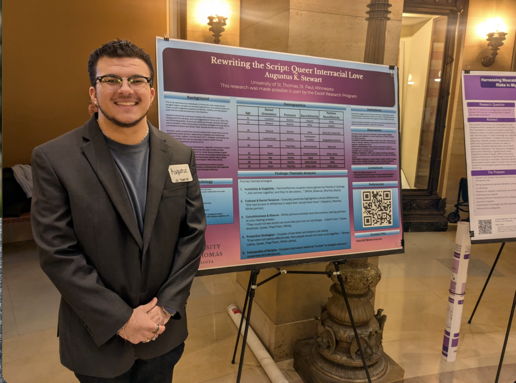 Augie Stewart stands next to a large poster that is titled "Rewriting the Script: Queer Interracial Love."