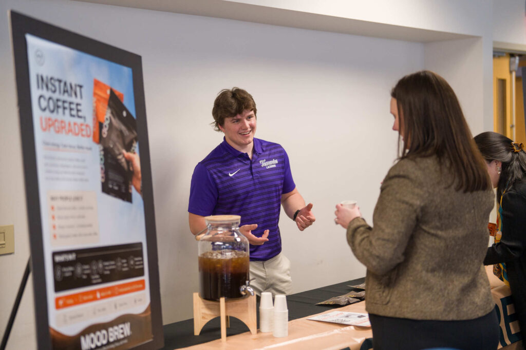 A student talking about his business at a station during eFest in front of people.