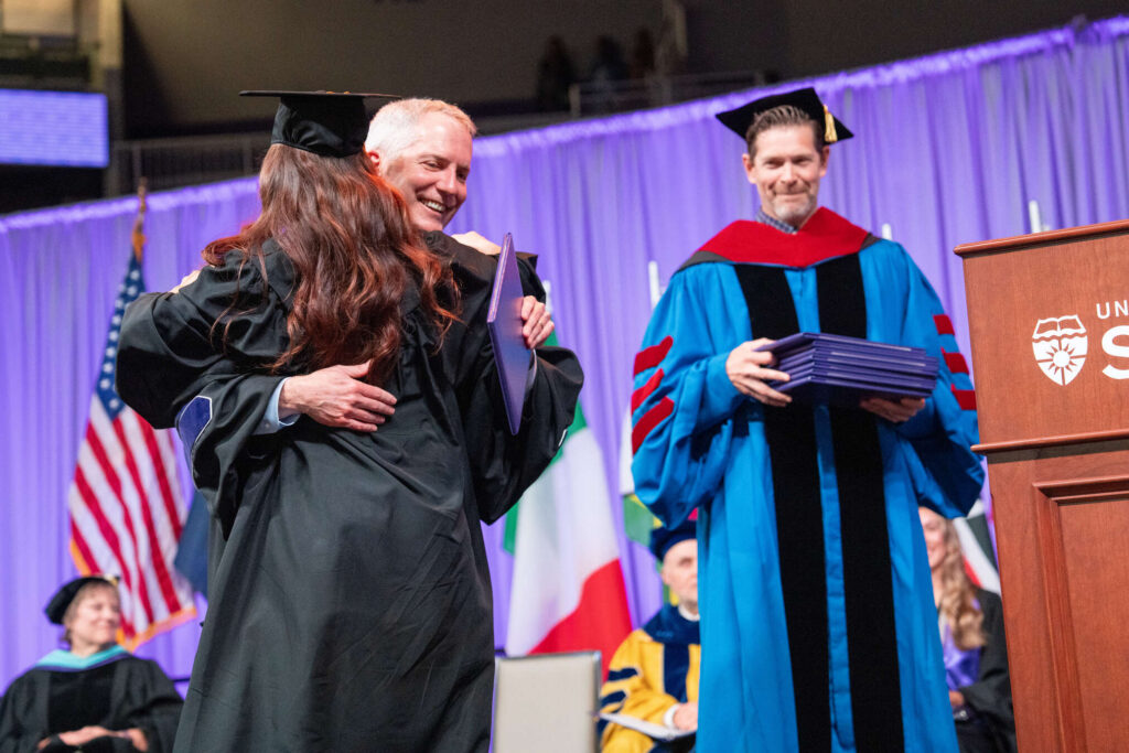 A graduate hugs President Rob Vischer during the 2026 College of Arts and Sciences Undergraduate Commencement Ceremony in Lee & Penny Anderson Arena in St. Paul on May 23, 2026.