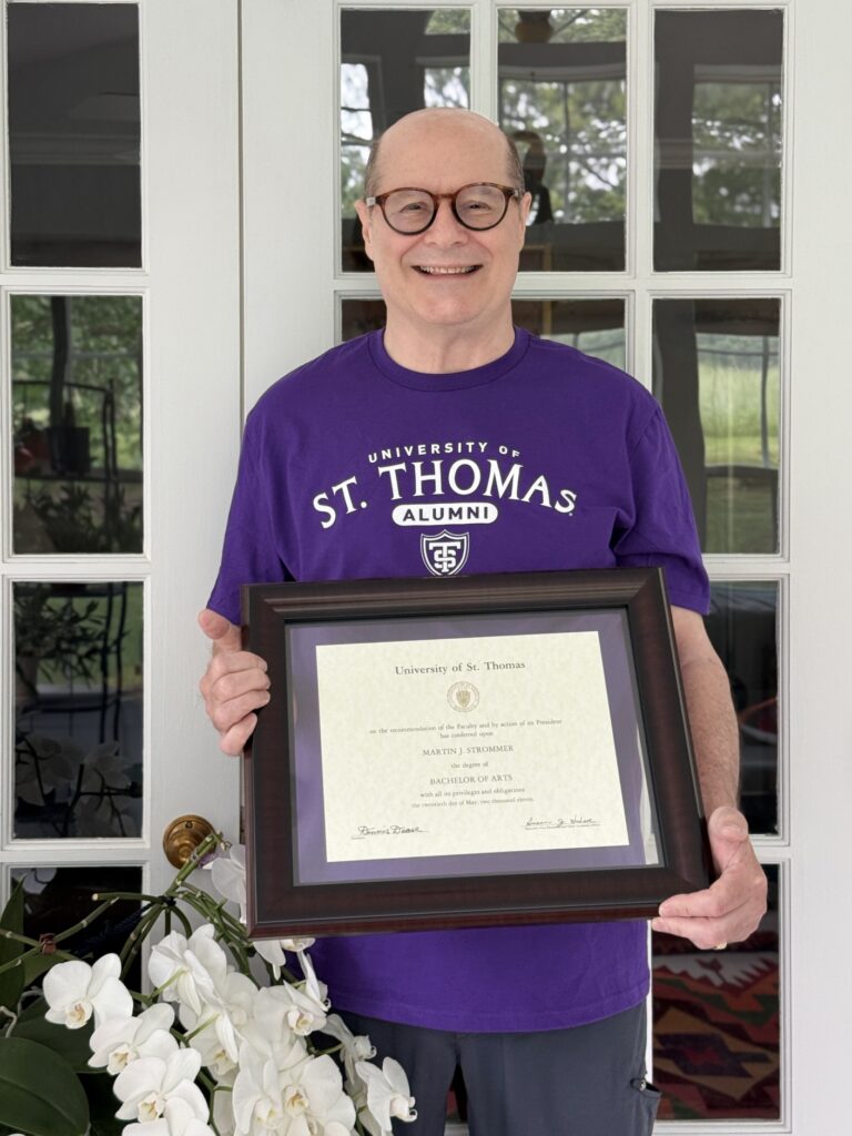 Martin Strommer smiles and holds his framed St. Thomas diploma.