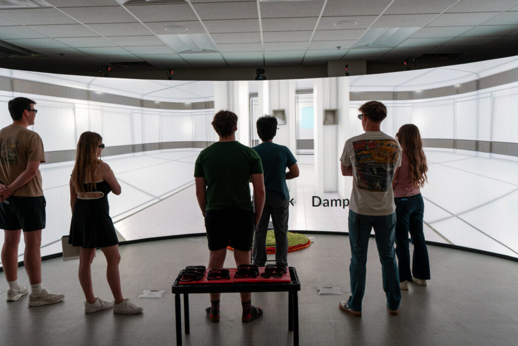 A guide and a group of students looking at a 32-foot semicircular screen to watch an elevator simulation.