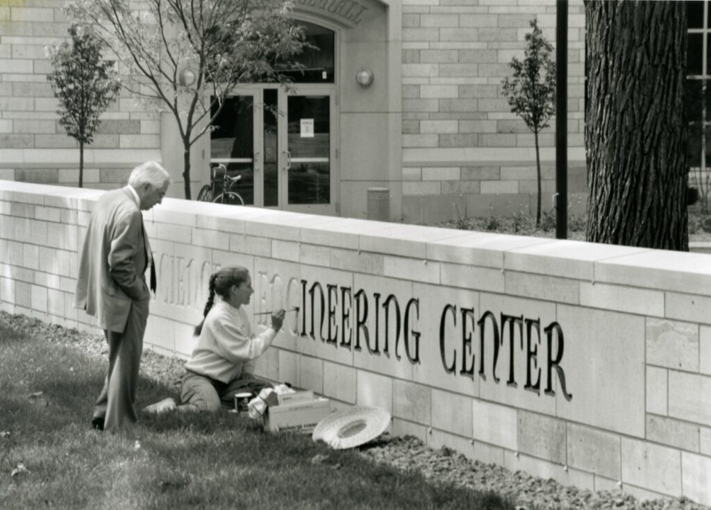 A lady painting the carved in letters of the Frey Science and Engineering Center.