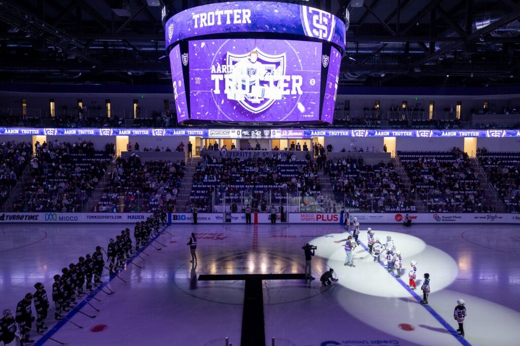 An overview look of the Lee & Penny Anderson Arena showing the Jumbotron, fan section and athletes lined up on the ice before puck drop.