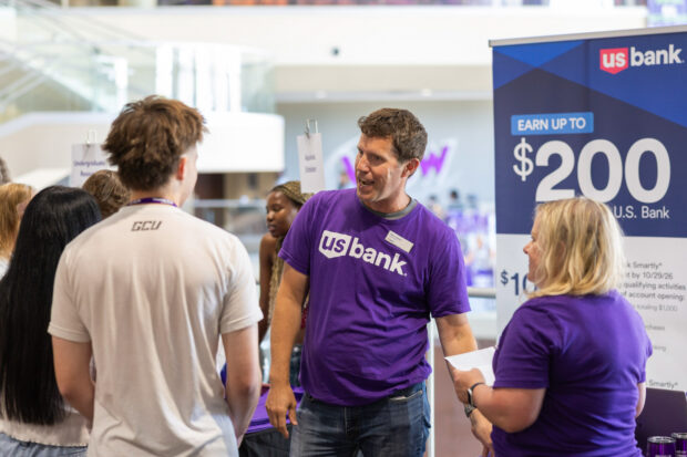 Students stand around a U.S. Bank booth on campus during a fair and speak to their reps.