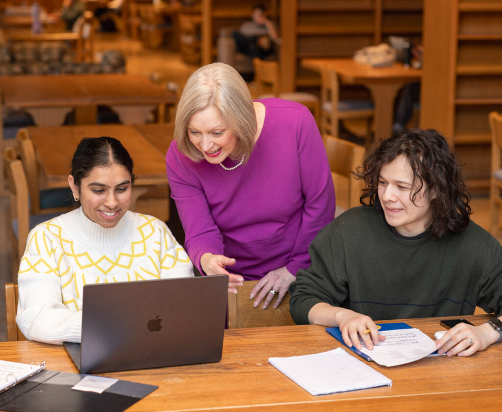 Amy Smith working with two students over their shoulder in a work space.