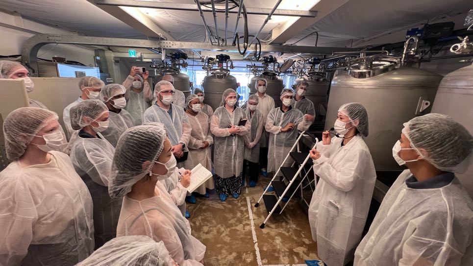 A group of graduate students gathered in a brewery with wearing masks and plastic caps covering hair.