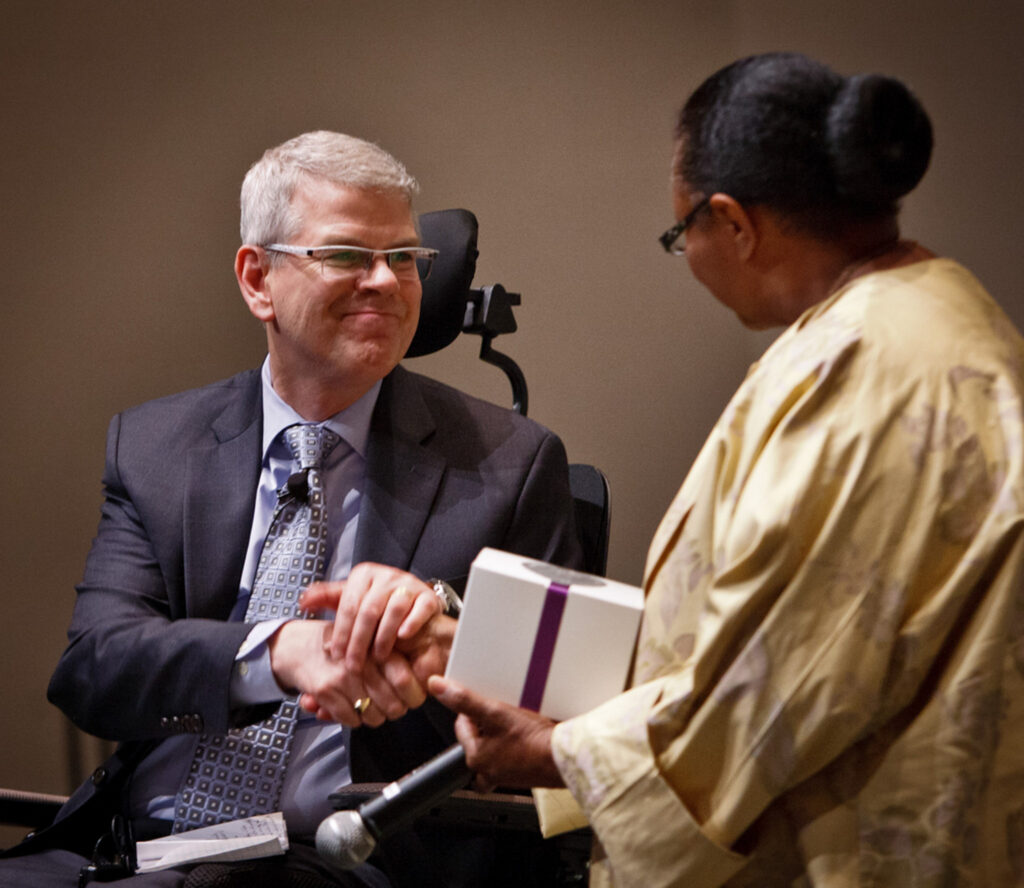 Bruce Kramer in a wheelchair shaking hands with Judge LaJune Thomas Lange.