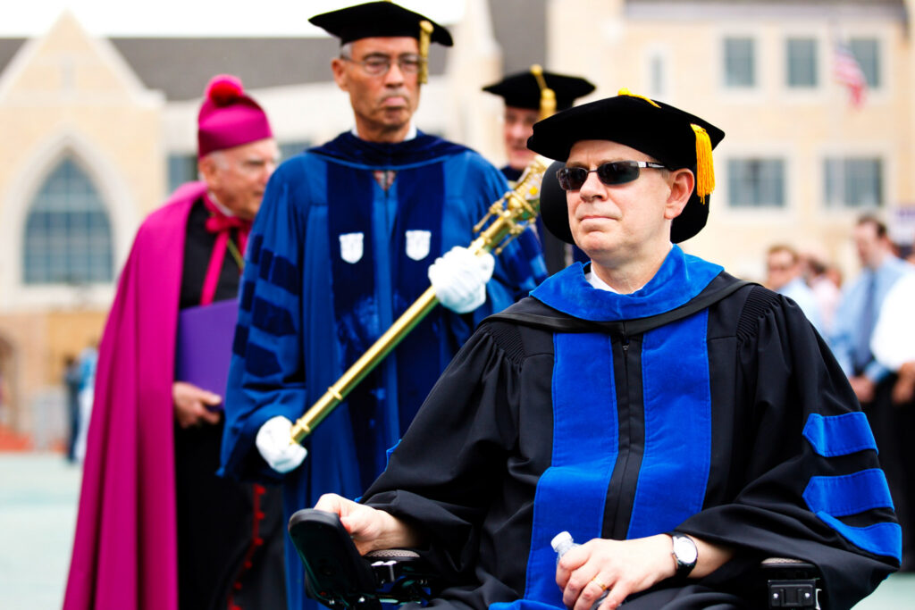 Bruce Kramer sitting in a wheelchair outside during a commencement ceremony.