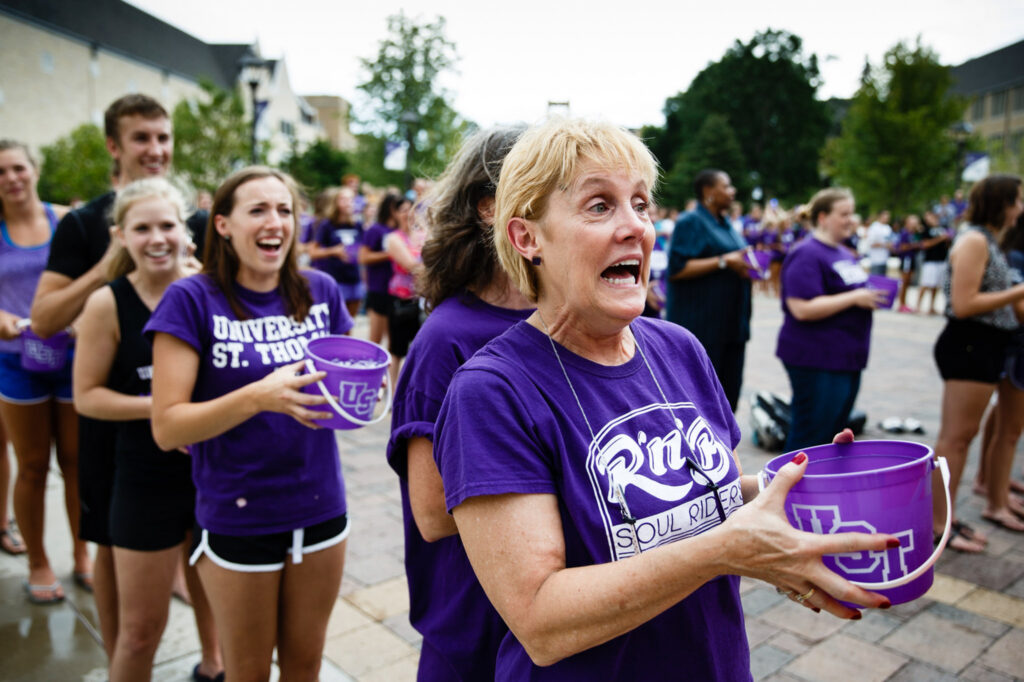 Lines of people wearing purple and holding a bucket outside on the campus of St. Thomas for the ice bucket challenge.