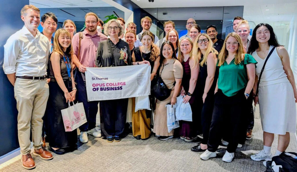 A professor and students pose for a group photo holding a St. Thomas Opus College of Business banner during an international travel trip in Asia.
