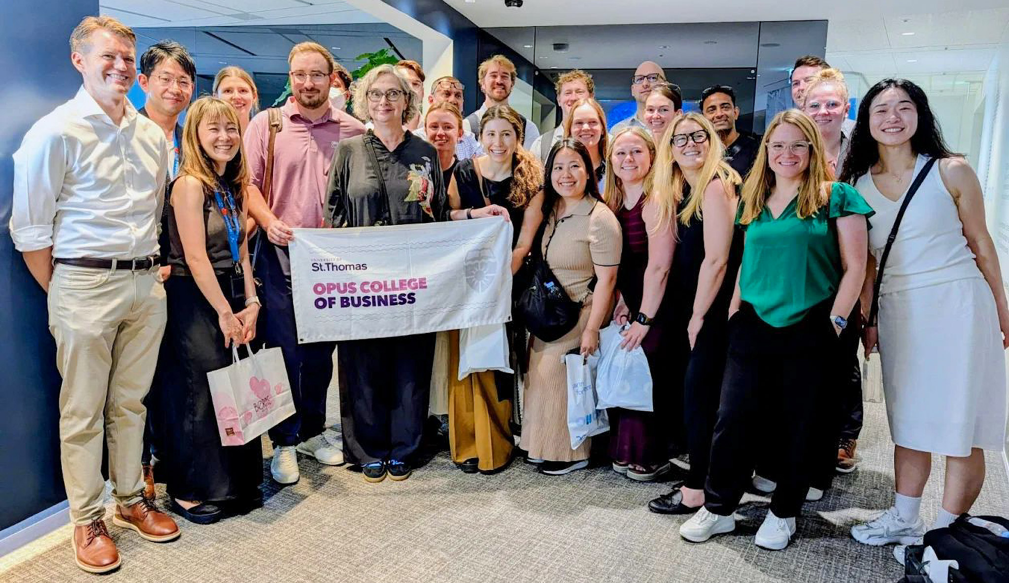 A professor and students pose for a group photo holding a St. Thomas Opus College of Business banner during an international travel trip in Asia.