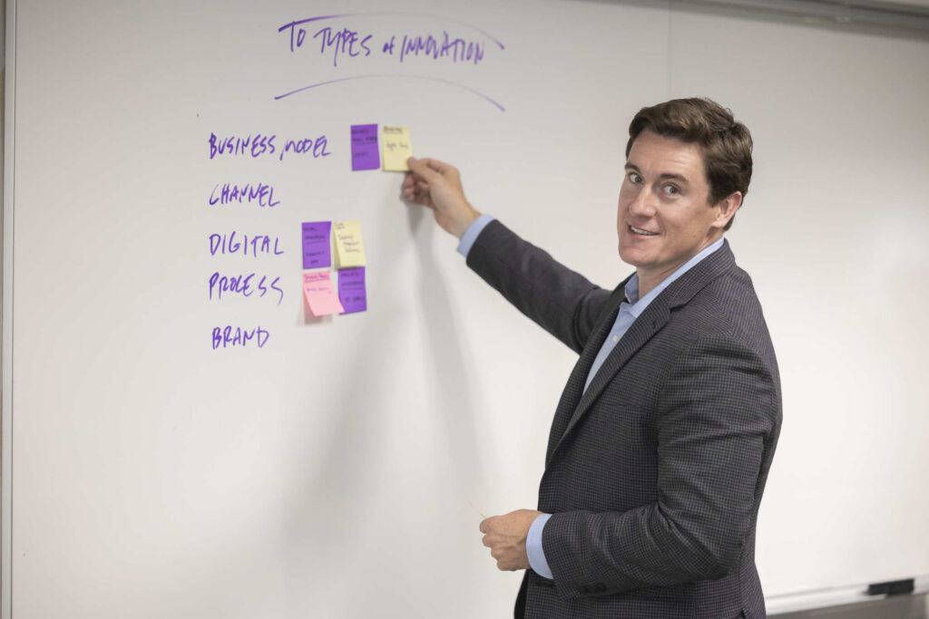 Sam Larson placing a post-it note on a white board while posing for a portrait.