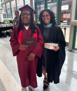 Two people standing next to each other with commencement gowns.