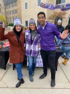 A group of three pose for a photo at a fair on campus.