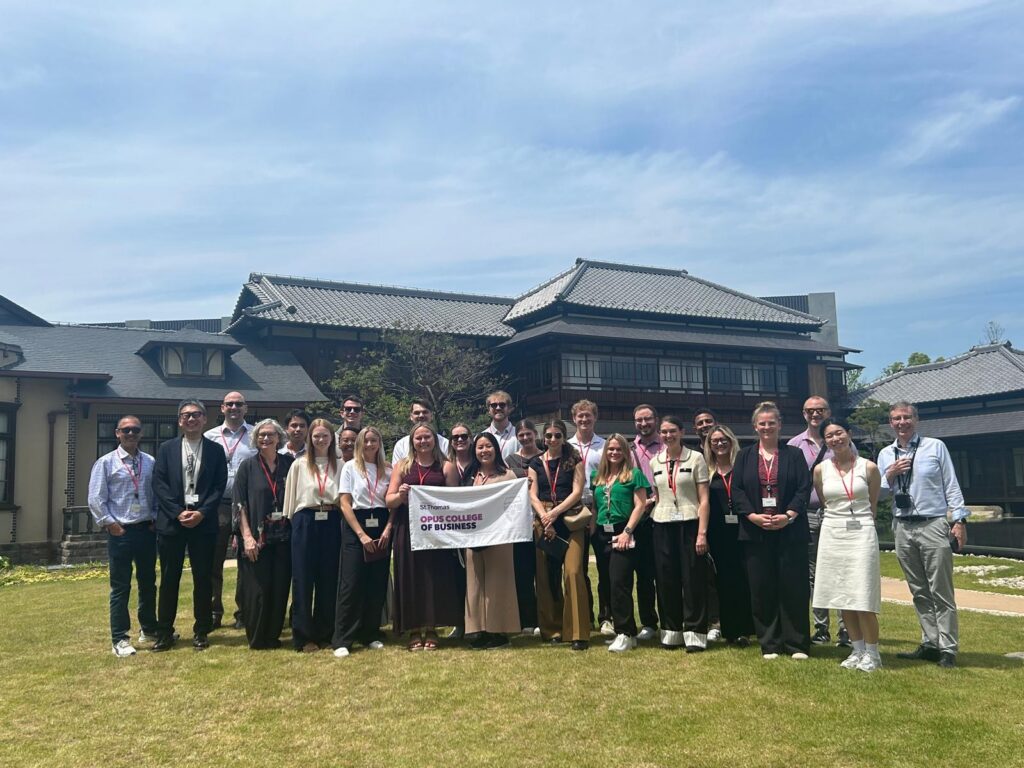 Graduates students hold an Opus College of Business banner in front of a building for Shimizu NOVARE in Tokyo, Japan.