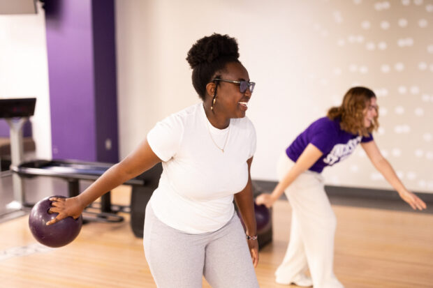 A student in the bowling alley in motion to release the bowling all down the lane.