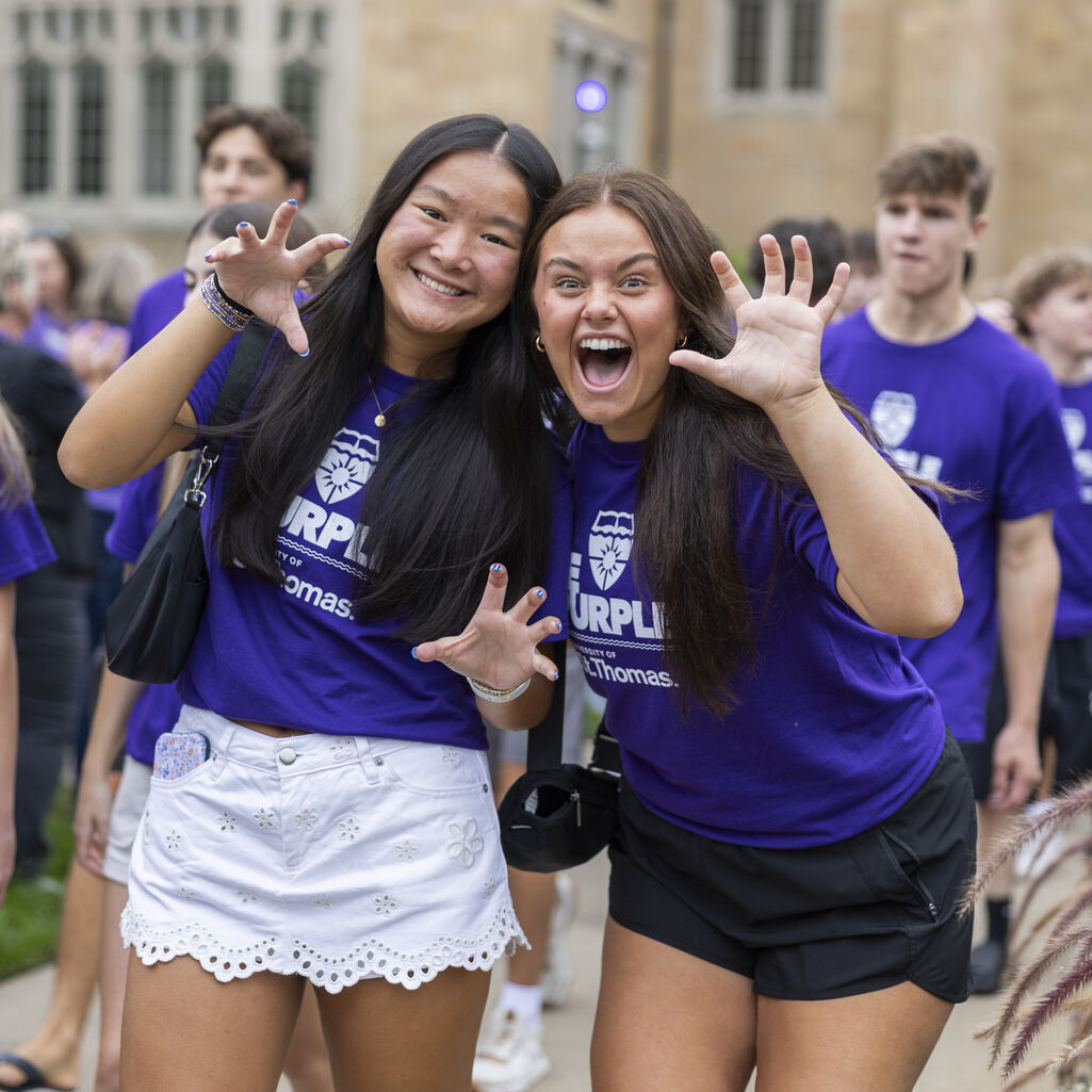 Two students smile while posing their hands in a claw fashion to imitate the Tommie claw.