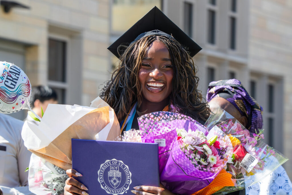 A student holding their diploma and flowers on DFC commencement day.