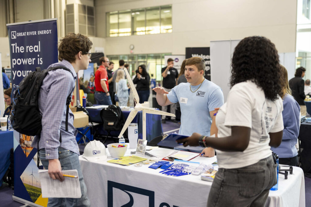 Two students stand at the Great River Energy booth to speak with a recruiter.